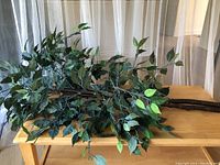 Close-up of large faux tropical plant branches with many dark green leaves spread out on a wooden table.