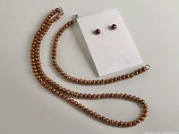 Necklace, bracelet, and pair of earrings displayed on white background showing bronze colored freshwater pearls and sterling silver findings.