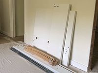 Disassembled white wooden and metal parts for IKEA MALM twin bed frame laid out against a wall showing multiple panels, rails, and wooden slats