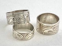 Three sterling silver bands with hand engraved Northwest Coast designs laid flat