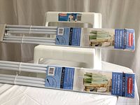 Two unopened Rubbermaid garment racks in original packaging placed on a white Rubbermaid plastic step stool.