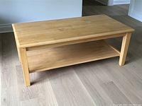 Top and side view of solid wood coffee table, showing rectangular table top and lower shelf with natural wood finish on light floor.