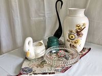 Photo showing various vintage home decor items arranged on the floral tapestry runner - includes ceramic swan planters, green canister, large floral vase, and glass bowl.