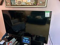 Front view of TV on glass stand with digital clock device and remote nearby