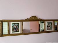 Full view of the antique rectangular gold framed mirror with ornate detailing and two framed decorative relief plaques on either side.