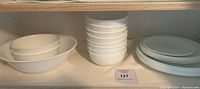 Shelved display of stacked white bowls, white large dinner plates, and two serving bowls on left.