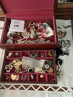 Photo showing two velvet-lined jewelry boxes, the upper holding assorted brooches and pendants, the lower divided with earrings, rings, and charms. Loose costume jewelry laid to the right including pendants and brooches.