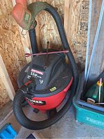 Red and black Craftsman 5.5 HP shop vacuum with flexible black hose and blower pipe placed on wooden floor in workshop.