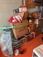 Photo of assorted packed boxes and bags containing Christmas decorations and other household items against a painted block wall beside an orange floor.