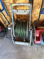 Full view of green garden hose coiled on a gray plastic hose reel stand with wheels and handle.