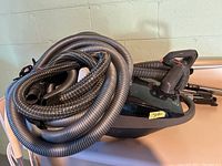 Kenmore vacuum cleaner with hose and attached tools coiled over it, placed on a beige surface.