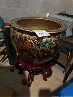 Large plant pot with grape and leaf painted design on a dark wooden stand, showing side view of the pot and stand