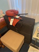 Folded massage table in black carrying case leaning against a wall with red face cradle and armrests placed on top