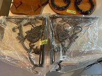 Pair of decorative cast iron plant brackets wrapped in plastic packaging on table with other metal items