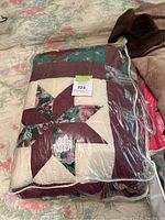 Folded queen size quilt featuring star and floral patchwork design, visible inside a clear plastic carrying bag.