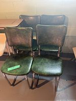 Photo of four dark green vinyl kitchen chairs grouped together showing textured vinyl seats and backs with chrome tubular metal frames in mid-century retro style.