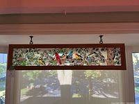 Front view of rectangular stained glass panel mounted in wooden frame featuring colorful birds and foliage.
