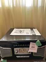 Front view of TEAC SL-A100 stereo system showing controls and speaker grills with owner's manual placed on top.