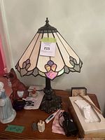 Tiffany style stained glass table lamp positioned on a wooden table surrounded by various small items.