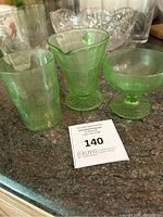 Three green uranium glass tumblers displayed on a countertop with auction lot number, showing their shape and color.
