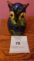 Front view of the vintage glass owl paperweight on a wooden surface with auction label in front.