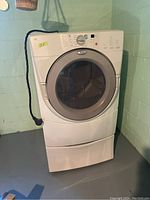 Main photo: front view of white Whirlpool front-load washing machine on pedestal in basement.