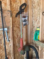 Image showing a Black & Decker electric weed whacker hanging on a wooden wall with a replacement spool or accessory in a plastic bag attached to it.