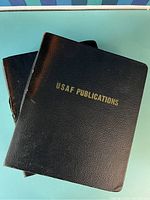 Two black binders with 'USAF Publications' embossed in gold on front covers, showing signs of wear and age.