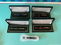 Overview of four Cross pen sets in black presentation boxes and one pen in molded plastic case with keyring accessory.