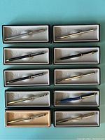 Overview of ten boxed Quill branded pens in various finishes and colors, arranged in pairs on blue background.