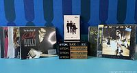 Photo showing three music CDs (Buddy Holly, Bon Jovi, The Beatles) and four sealed TDK cassette tapes in black and gold packaging.