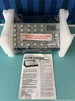 View of the Sound System II controller unit with multiple knobs and switches, packaged with instruction sheet and protective foam.