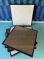 Stack of four black square vinyl album frames with glass front, visible reflections, and black edges.