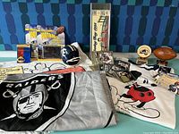 Photo of the entire lot laid out showing the Raiders flag, Mickey Mouse t-shirt, wooden collectibles, and NFL cards