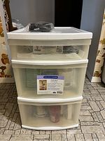 Full frontal view of the white 3-drawer plastic storage unit with visible contents in drawers and top surface items.