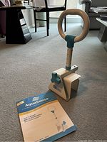 Photo showing white and blue steel bath safety rail with adjustable height and user manual on carpeted floor.
