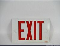 Photo of a single Beghelli Quadra Exit Light showing white housing with red EXIT lettering and left and right removable chevron arrows.