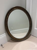 Front view of the oval mirror showing the detailed silver painted wooden frame and reflective surface, placed against a beige wall and carpet.