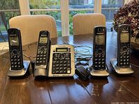 Full view of the Panasonic KX-TG7641 phone system including base phone unit and three cordless handsets placed on a wooden table.