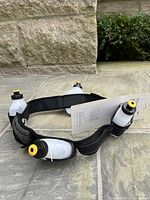 Running hydration belt laid out, showing black padded adjustable belt with three clear no-look click-in water bottles with yellow and black caps attached.