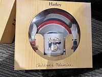 Hatley melamine children's dinner set featuring drum set graphic on mug, includes plate, bowl, mug with two handles, spoon, and fork, in box.