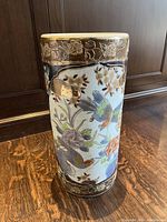 Front view showing bird and floral designs with gold accent around rim and base, standing on wooden floor against dark wood furniture
