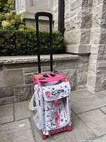 Front view of Zuca skating bag with extended black luggage handle, pink aluminum frame, white and pink patterned polyester, and mesh side pocket.