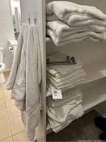 Full view of the white towels folded on bathroom shelving and two bath towels hanging on hooks on the bathroom door.