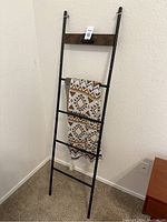 Photo of black metal blanket ladder with wooden top brace and southwestern style throw hanging, in a carpeted corner.