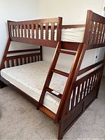 Full side view of the wooden bunk bed showing full size bottom mattress and twin top mattress with angled ladder attached