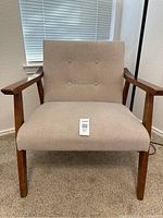 Front-facing view of the beige fabric accent chair with wooden arms and legs placed on carpeted floor.