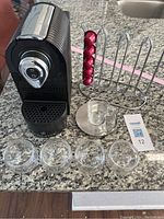 Front view of black ChefWave espresso machine with pod holder loaded with five red coffee capsules, five double-walled glass espresso cups, and one glass cup on saucer with spoon.