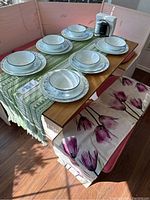 Corelle dinner plates, salad plates, and bowls arranged on a wooden table with green and purple floral table runners, also visible is the pink floral bench seating.