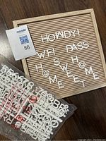Wooden framed letter board sign with white plastic letters arranged partially to spell 'HOWDY', 'WFI', 'PASS', 'HOME', and other letters scattered; includes multiple white plastic letters and characters in bags beside the board.